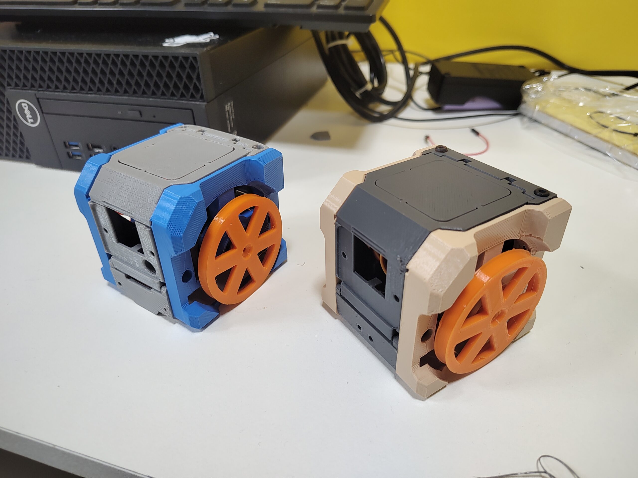 Dois chassis decabot impressos em 3D, um azul com cinza, outro creme com cinza, ambos com rodas laranja.